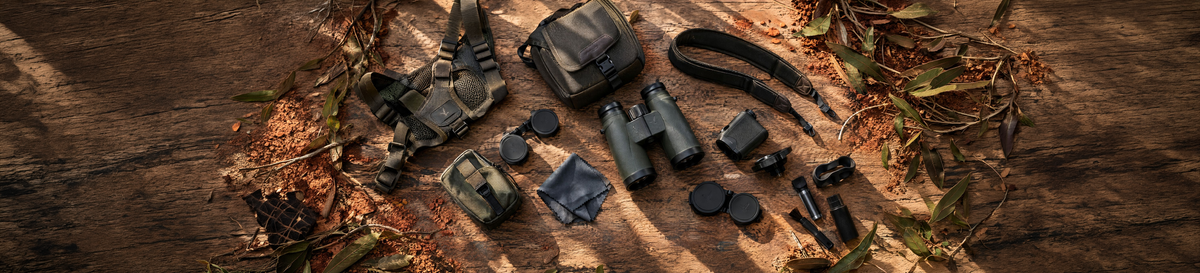 Binoculars with harness, cases, lens caps, strap, cleaning cloth and rangefinder laid out on timber
