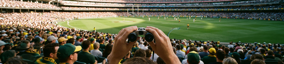 Sports fan holding compact binoculars at a packed cricket stadium
