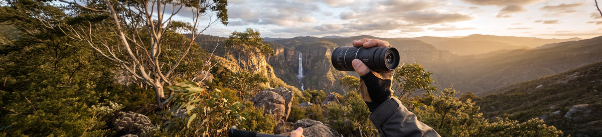 Hiker holding a monocular above a waterfall gorge in the Australian bush at sunset